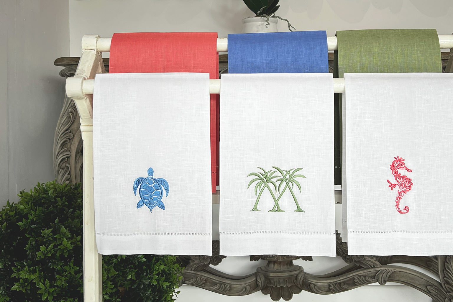 Embroidered linen hand towels featuring turtle, palm, and seahorse motifs in red, blue, and green by Pink House Mustique.
