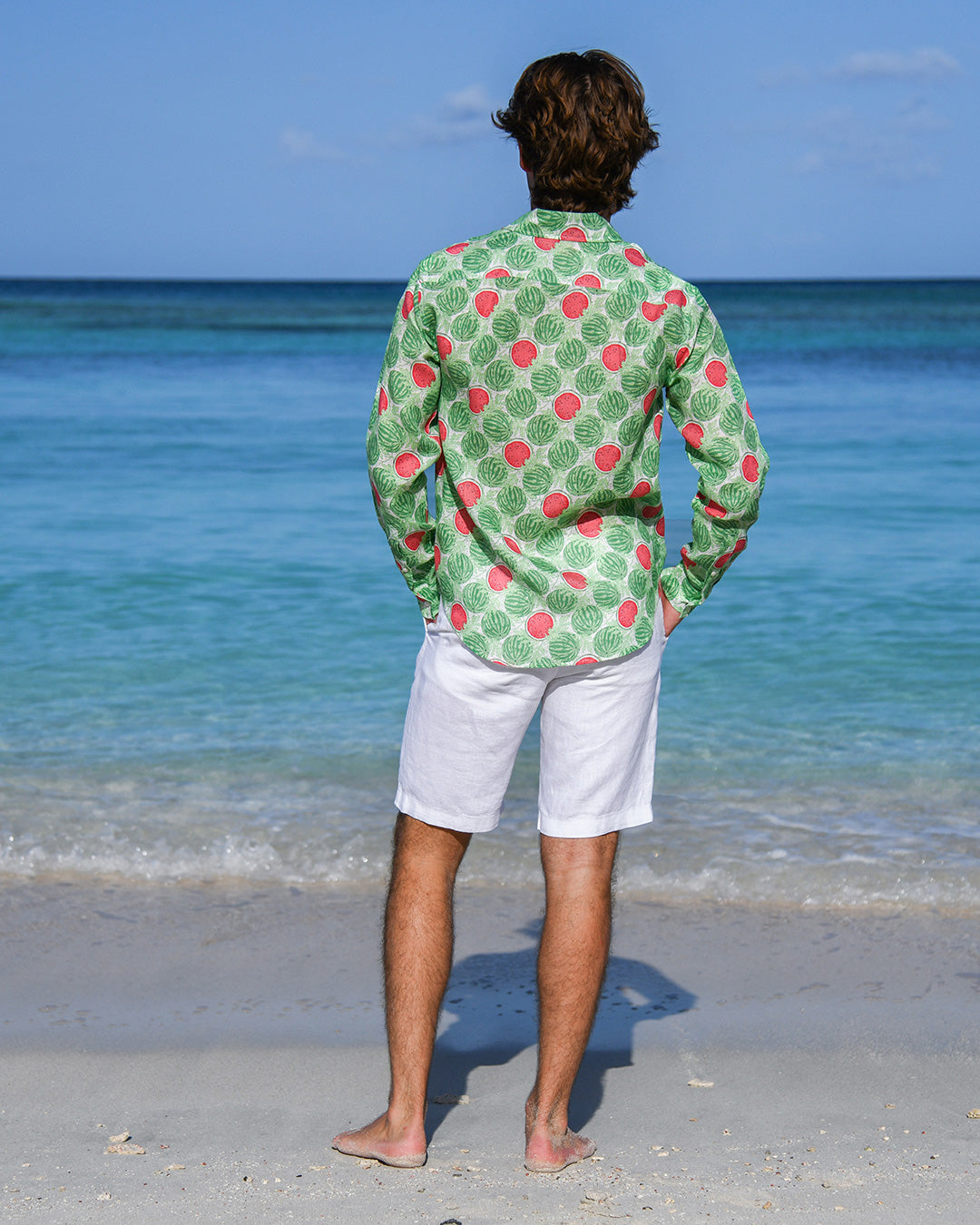 Back view of man wearing Watermelon Green linen shirt with white shorts on a tropical beach