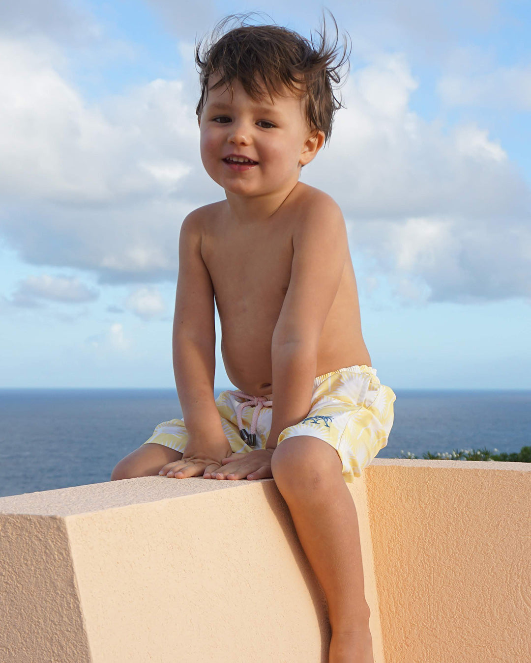 Young boy wearing Fan Palm Yellow swim shorts overlooking the sea in Mustique