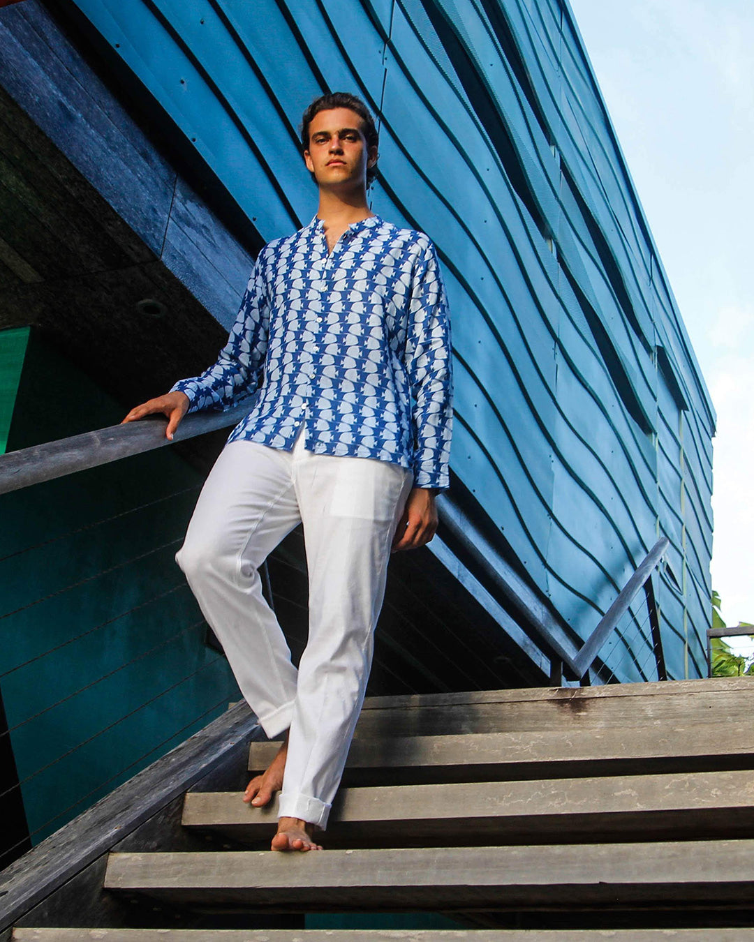 Male model wears Pink House Mustique collarless linen shirt in Fish print Airforce Blue – lightweight resortwear shirt styled with white trousers, ideal for tropical holidays and relaxed summer evenings.