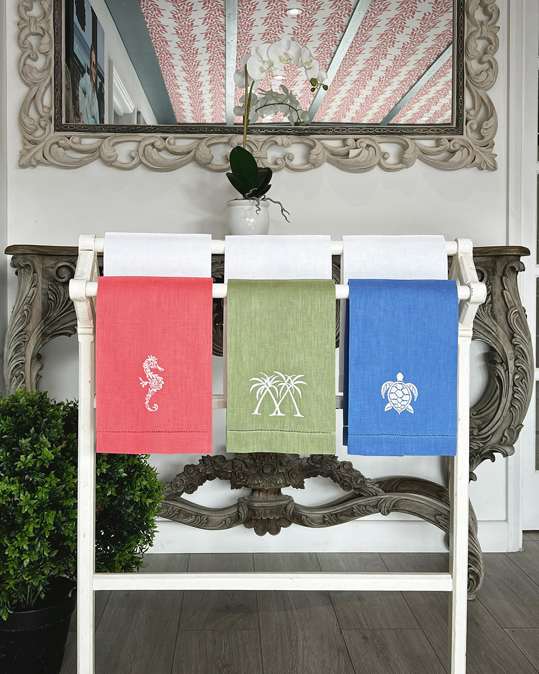 Coloured linen hand towels with embroidered seahorse, palm, and turtle motifs displayed in Pink House Mustique showroom.