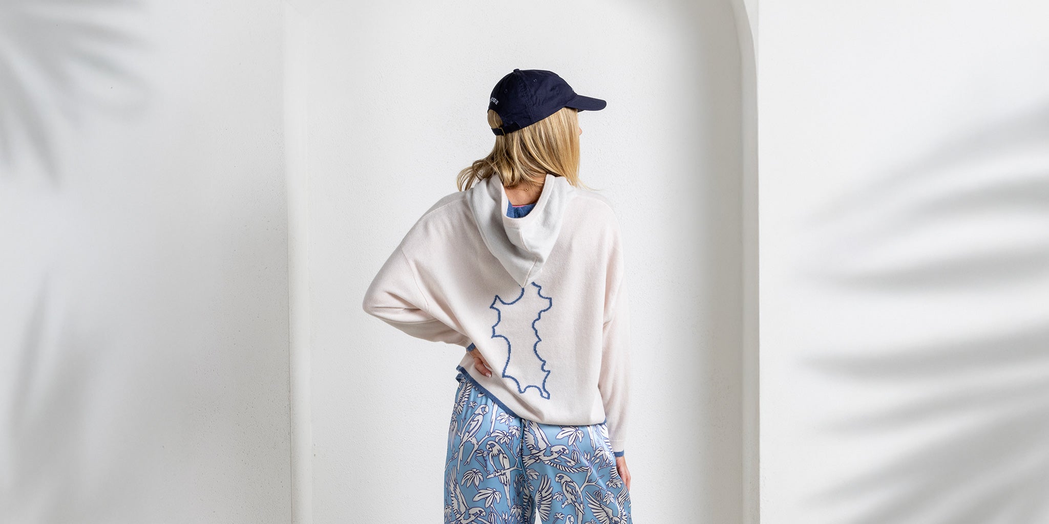 Back view of silk PARROT blue pajama pants styled with beige cashmere Mustique hoodie, islandwear by Lotty B