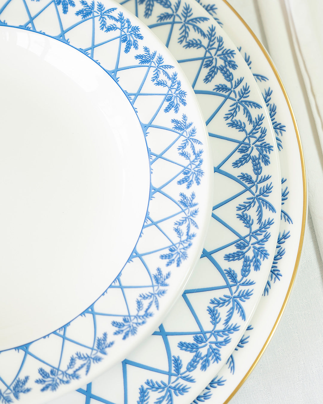 Close-up of fine bone china Palms Azure Blue rimmed bowl with Coconut Blue plate stack and gold detailing.