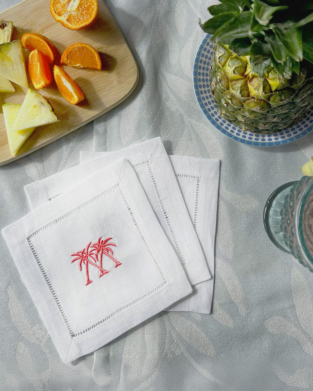 Embroidered linen cocktail napkins in Palms coral pink styled with fruit on a tropical table setting