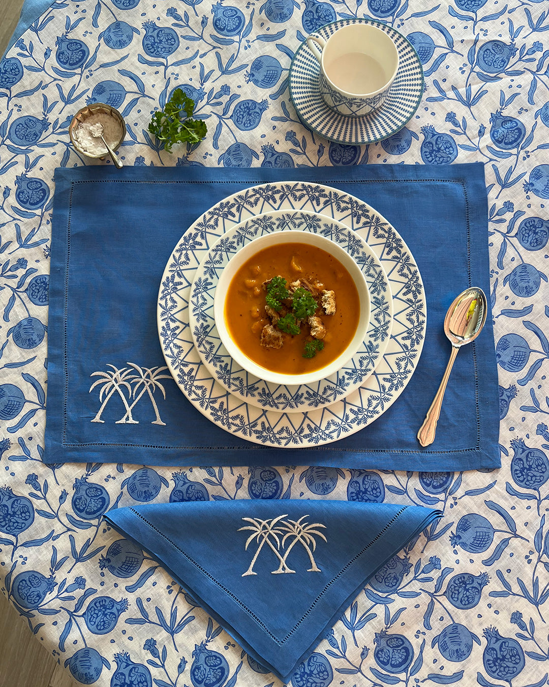 Embroidered linen placemat in Palms Azure Blue with matching napkin, styled with fine bone china tableware