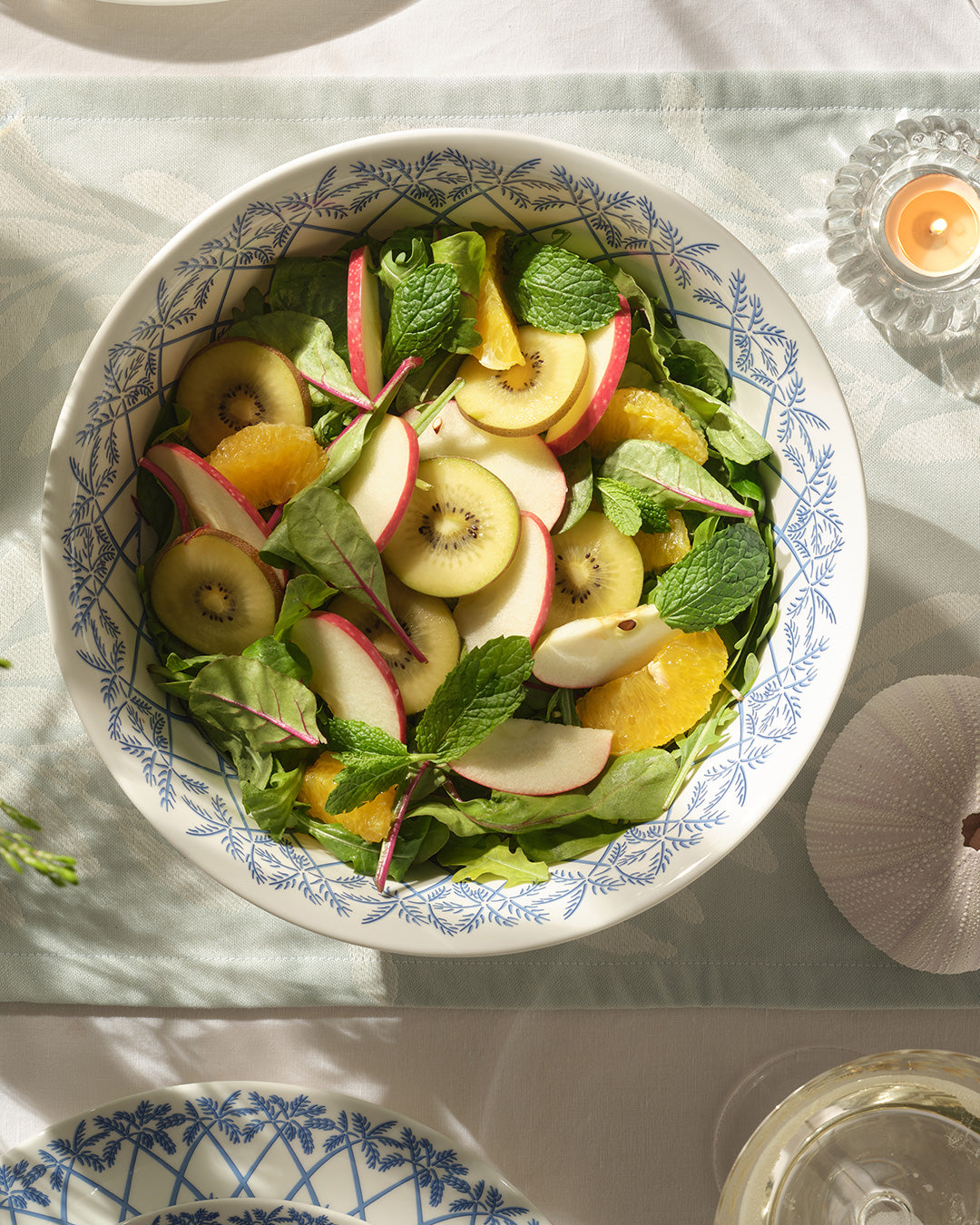 Fine bone china round serving bowl in Palms Azure Blue with fresh kiwi, orange and apple salad – luxury island style tableware