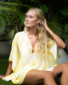 Woman wearing a yellow and white silk kaftan cover-up against a tropical background