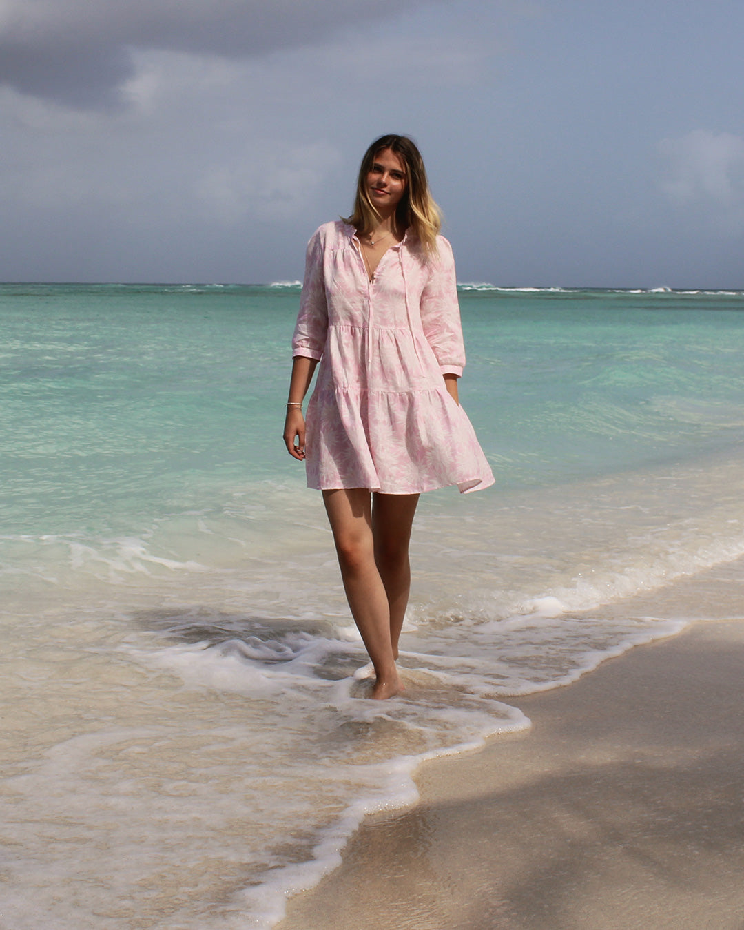 Amy linen tiered dress in Agave pink modeled by Yumyum on Lagoon Beach Mustique – relaxed luxury island style.