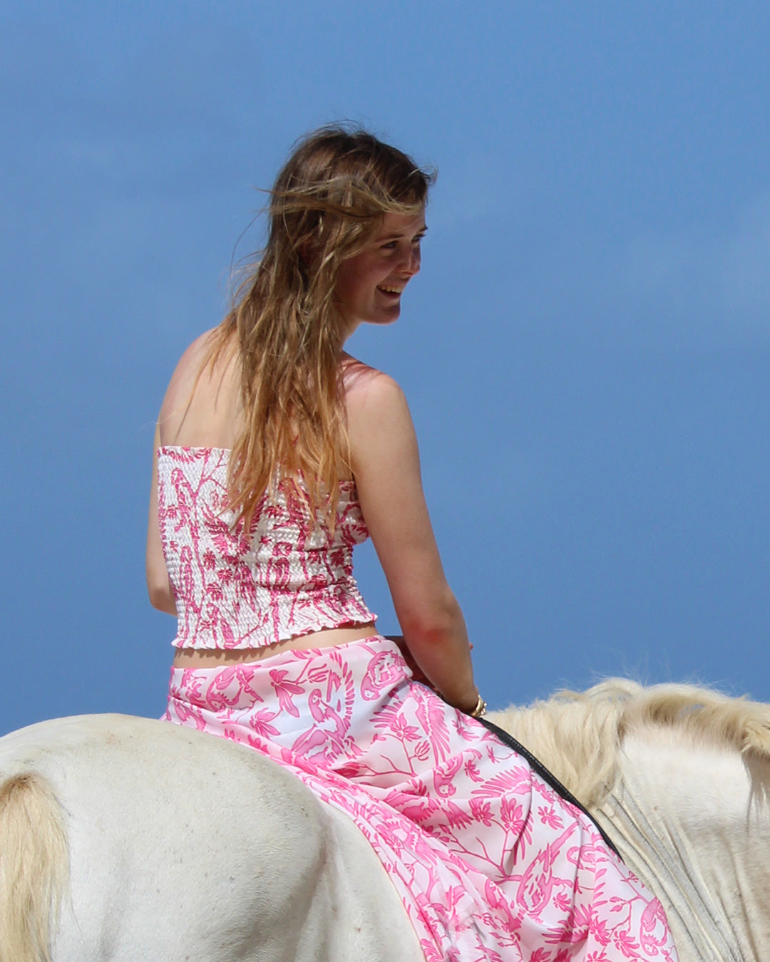 Back view of silk Parrot Pink ruffle bandeau top and sarong worn horseback on Mustique – designer beachwear style
