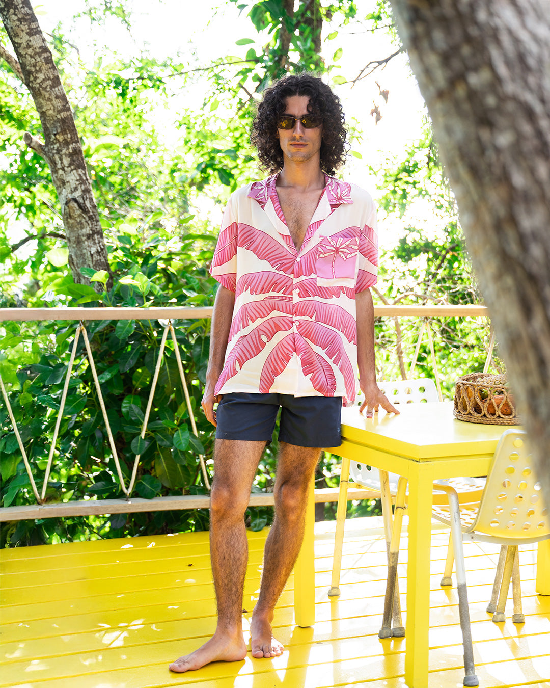 Men's silk Festival Shirt in Banana Tree Pink by Lotty B, styled with navy swim shorts on Mustique villa terrace
