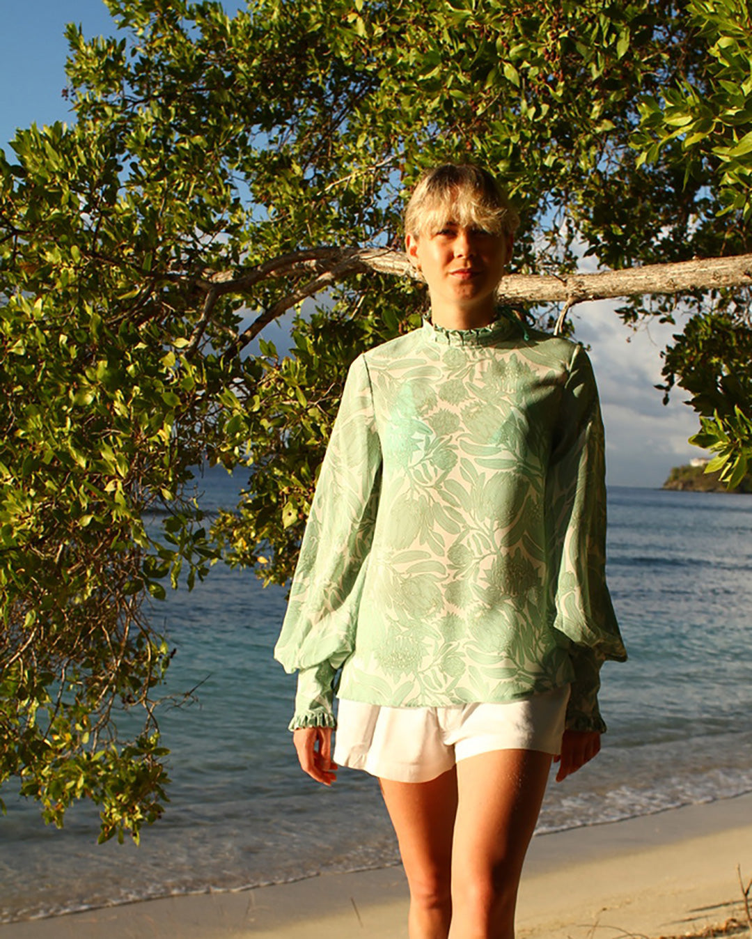 Mustique island style pure silk Kelly blouse in Protea sage green and white worn with classic white linen shorts by designer Lotty B for Pink House