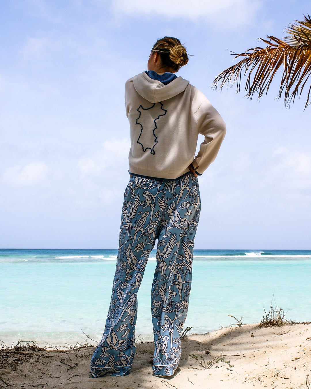 Pure silk pajama pants in parrot blue with Mustique Island cashmere hoodie worn beachside on Lagoon Bay