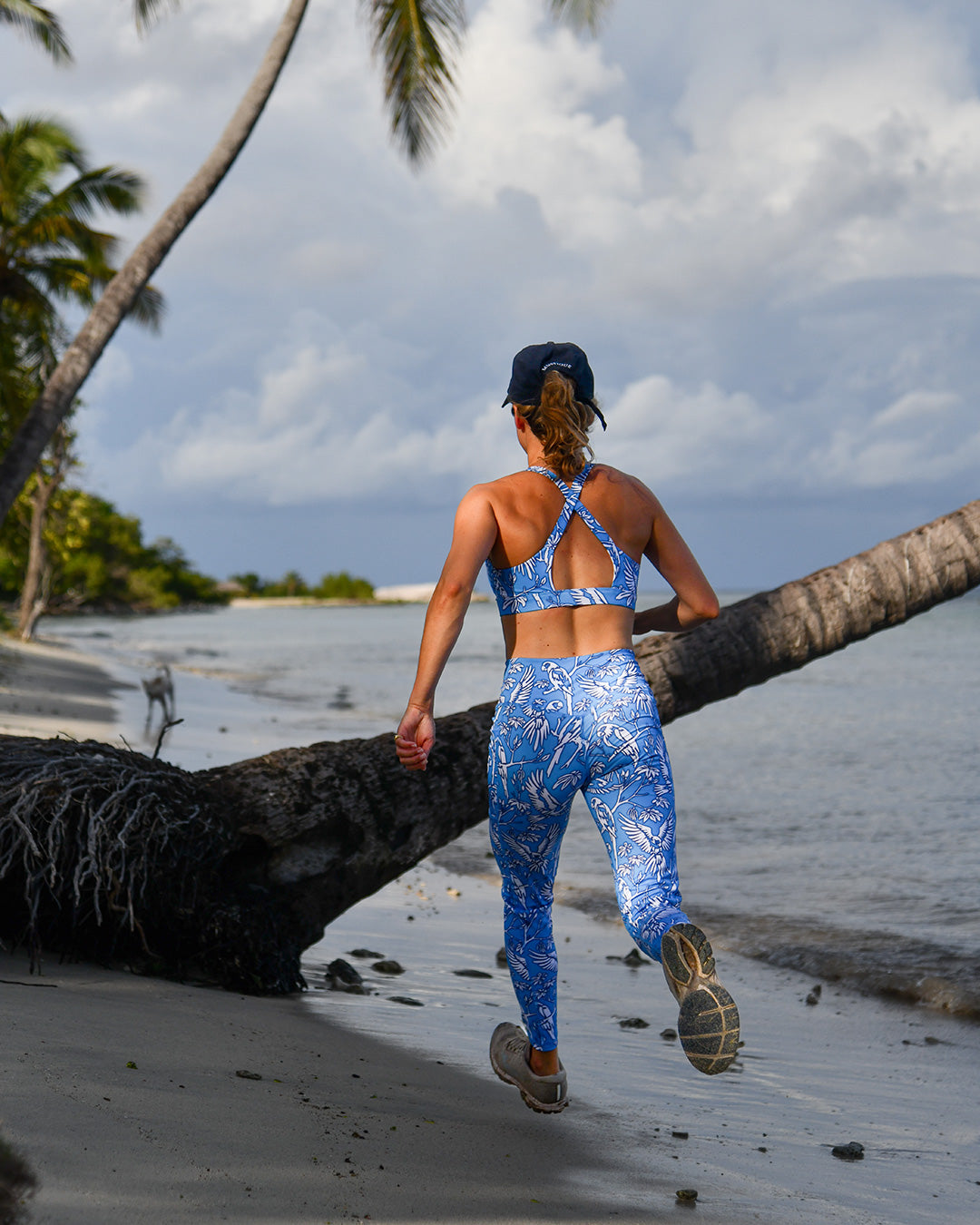 Running lifestyle photo of Madeleine in Parrot Blue criss-cross cropped sports bra top and leggings on Mustique beach