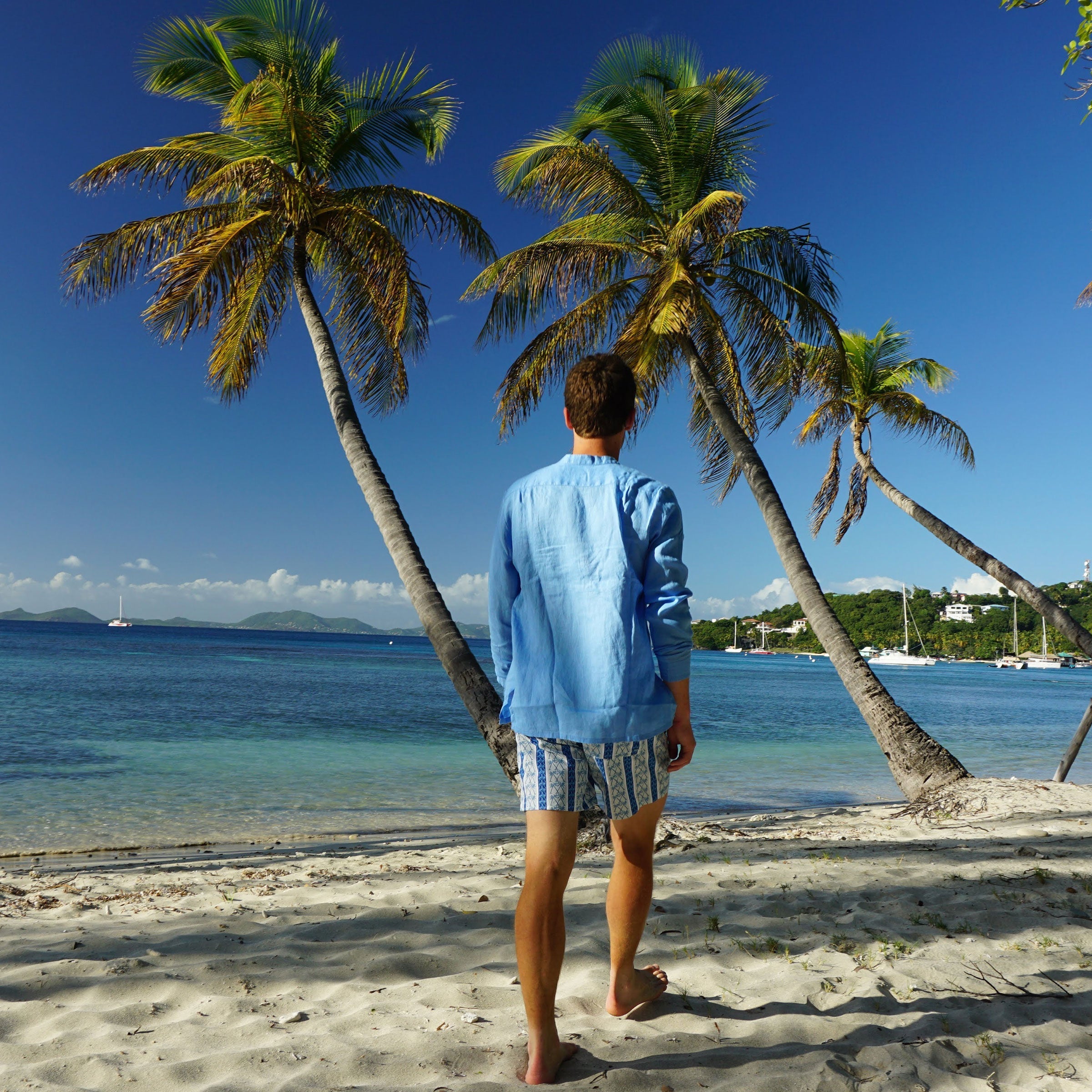 Mens swim shorts in NAVY PALM STRIPE walking on Britannia Bay Mustique