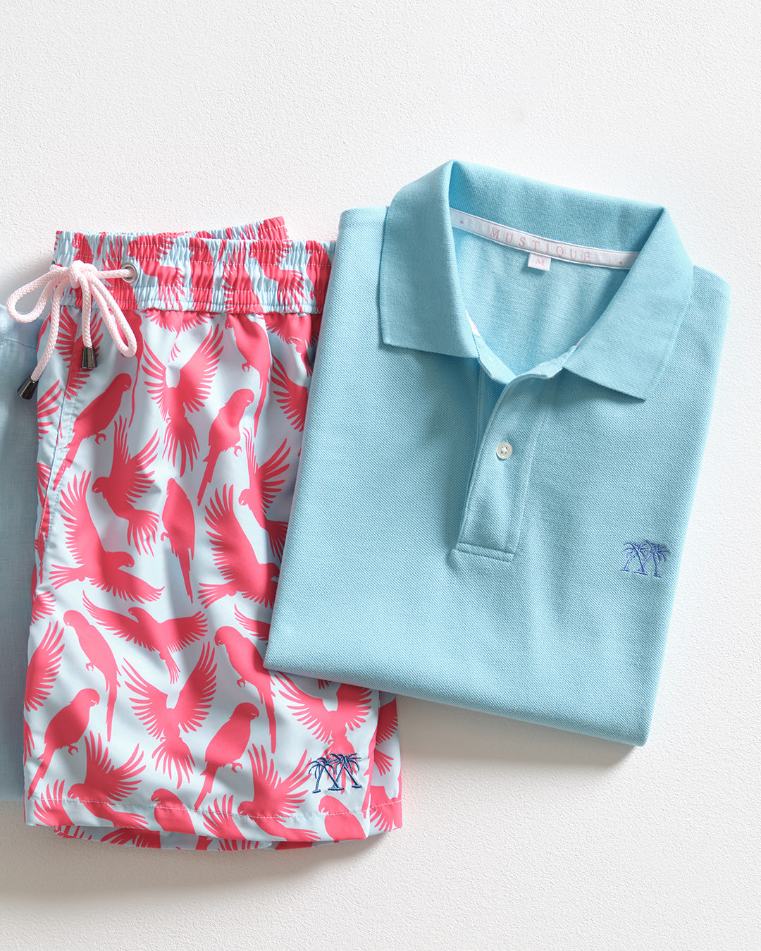 Pink House Mustique pale blue cotton polo shirt styled with pink Parrot print men's swim shorts