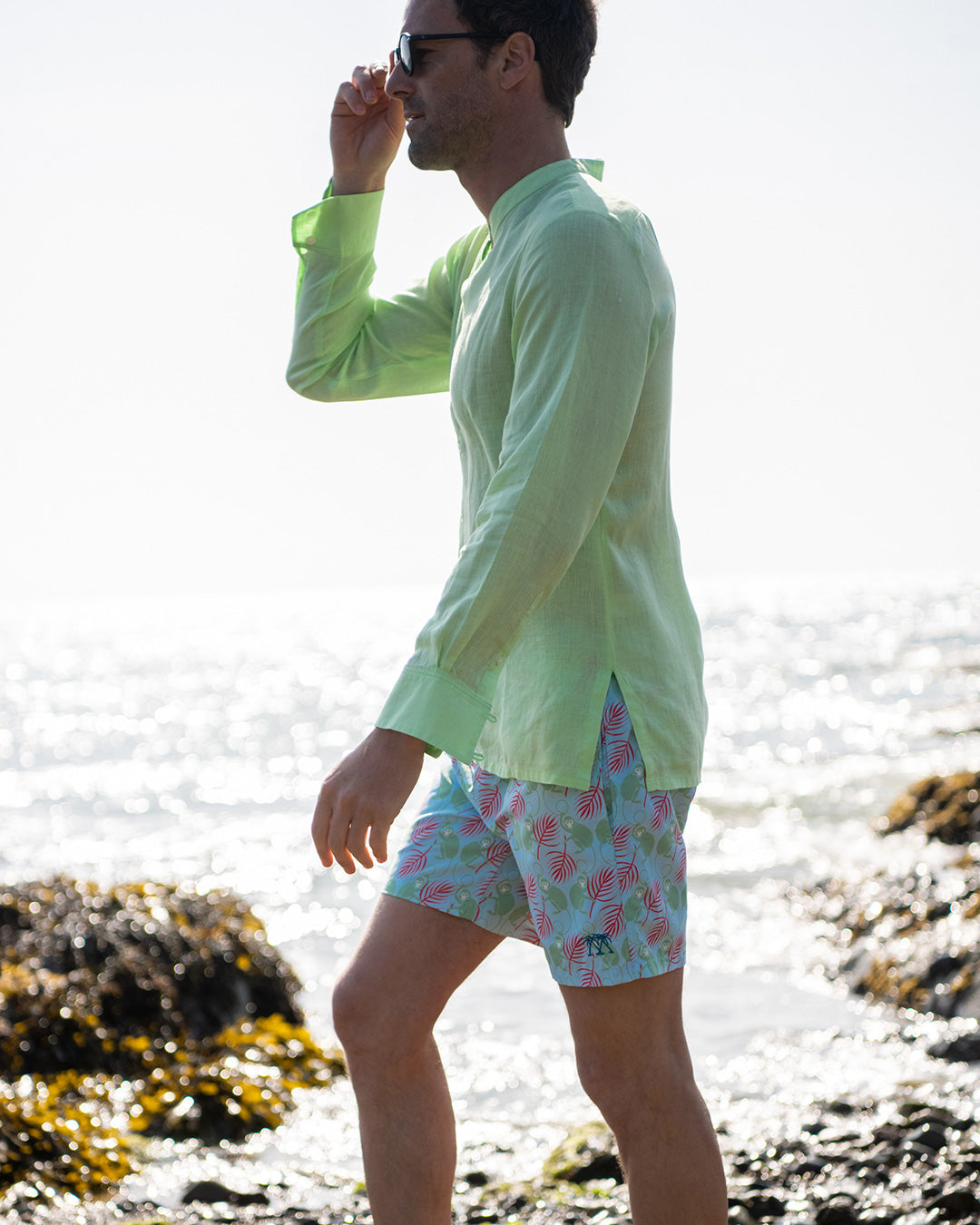 Mens pistachio green linen collarless shirt side profile on beach, grandad Nehru style with patterned swim shorts
