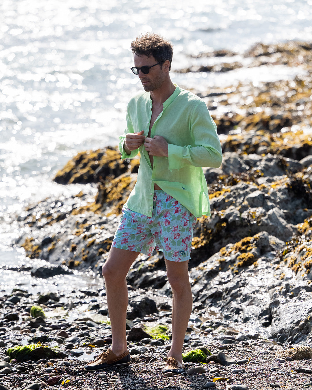 Mens pistachio green linen shirt with collarless grandad Nehru collar, buttoning on beach with green pink swim shorts