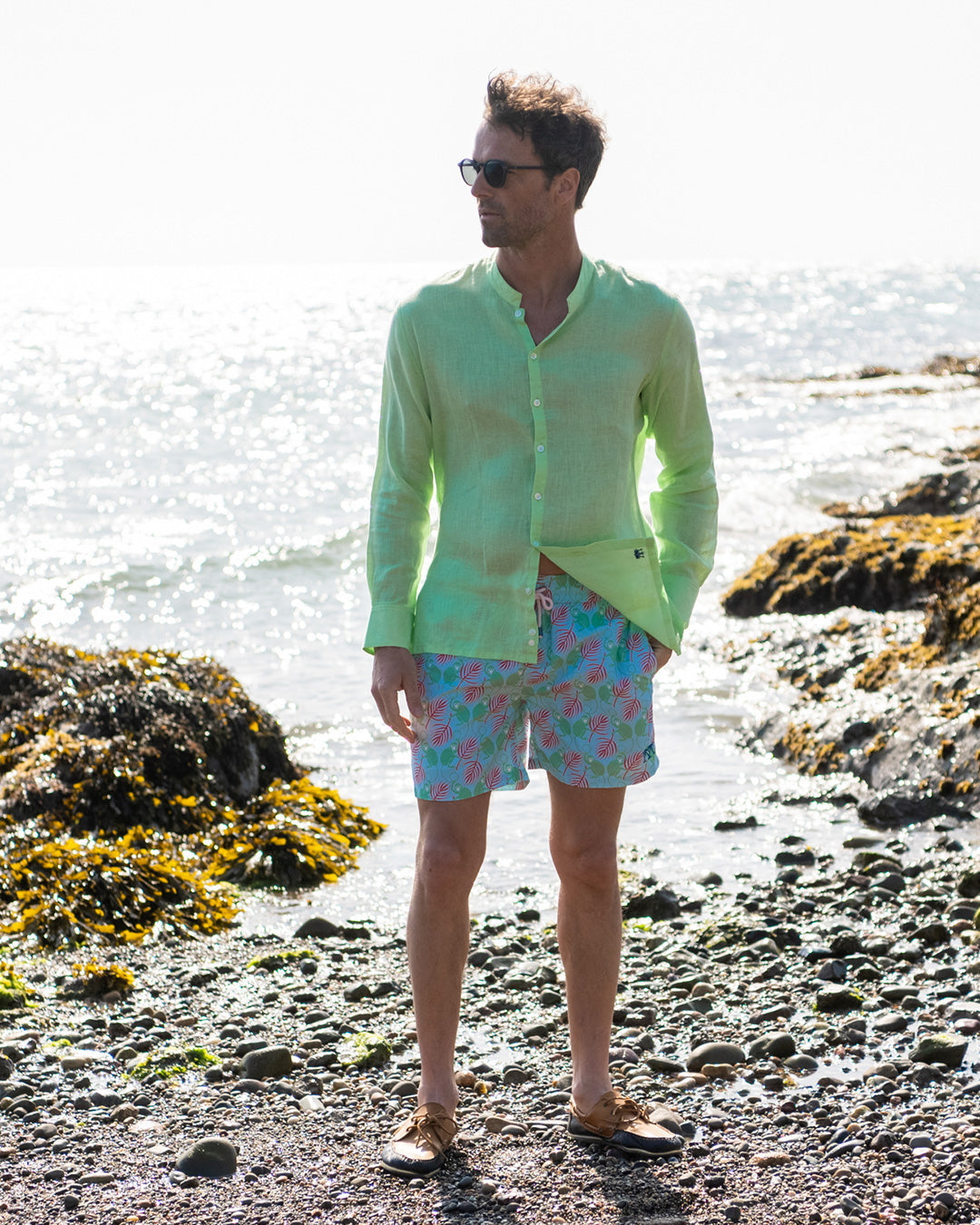Mens pistachio green linen shirt with grandad Nehru collar styled with green pink monkey print swim shorts on beach