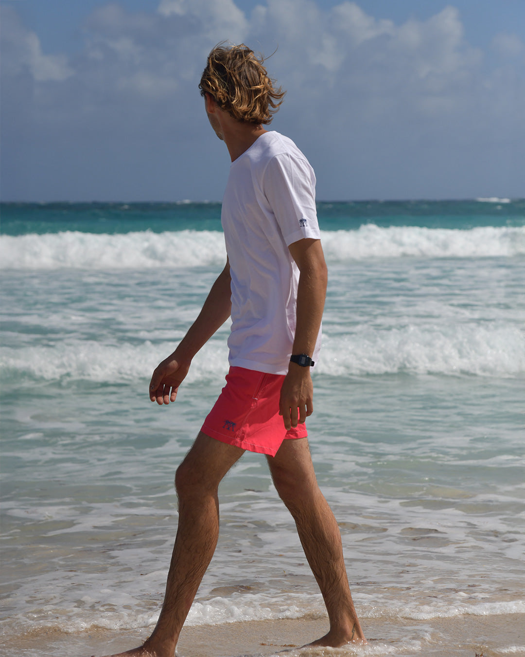 Men's white cotton T-shirt and faded red swim shorts walking along the shoreline in Mustique
