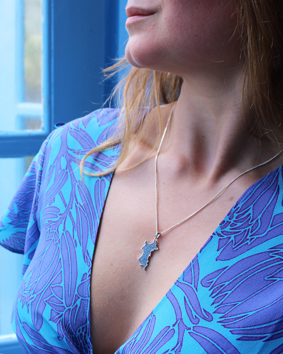 Sterling silver mini Mustique island pendant necklace with blue zirconia crystals worn with turquoise silk top Made in England