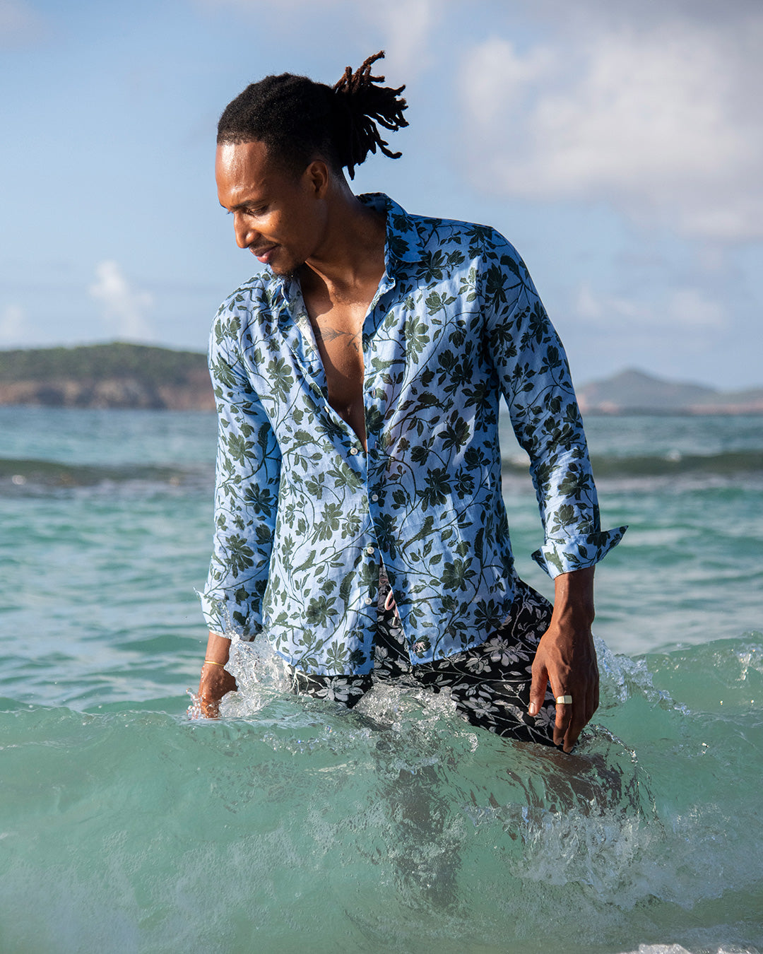 Men’s Iguana linen shirt in blue spruce green by Pink House Mustique, wading in turquoise Caribbean sea.