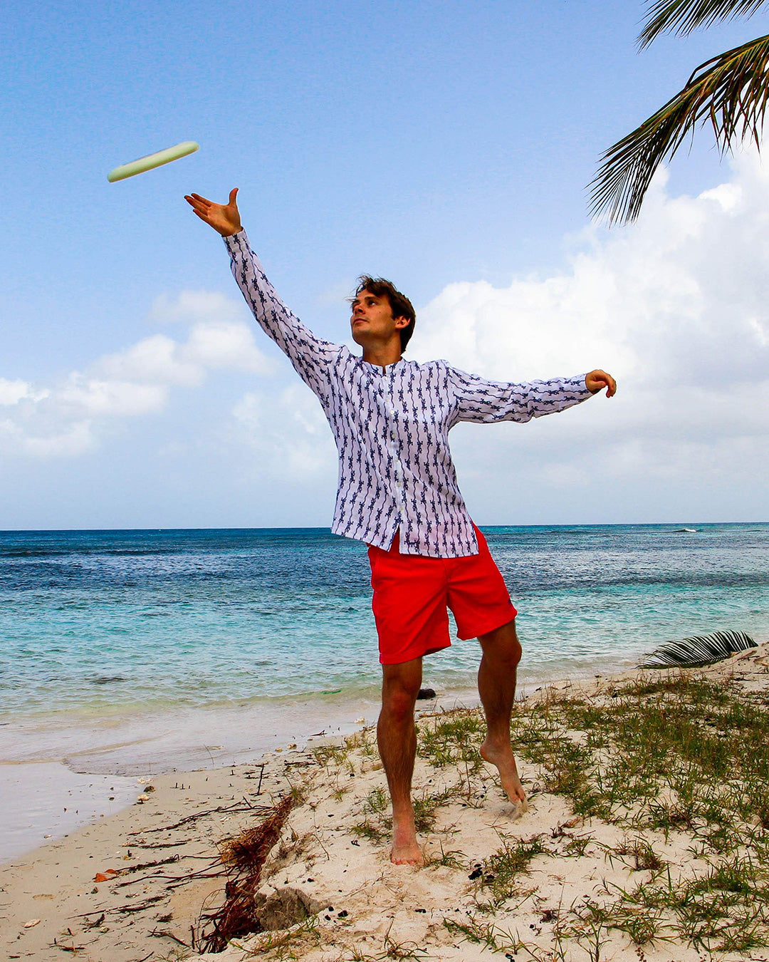 Fabian wearing Pink House Mustique collarless linen shirt in Gecko Navy print paired with red swim shorts – lightweight breathable resortwear ideal for beach holidays and tropical climates.