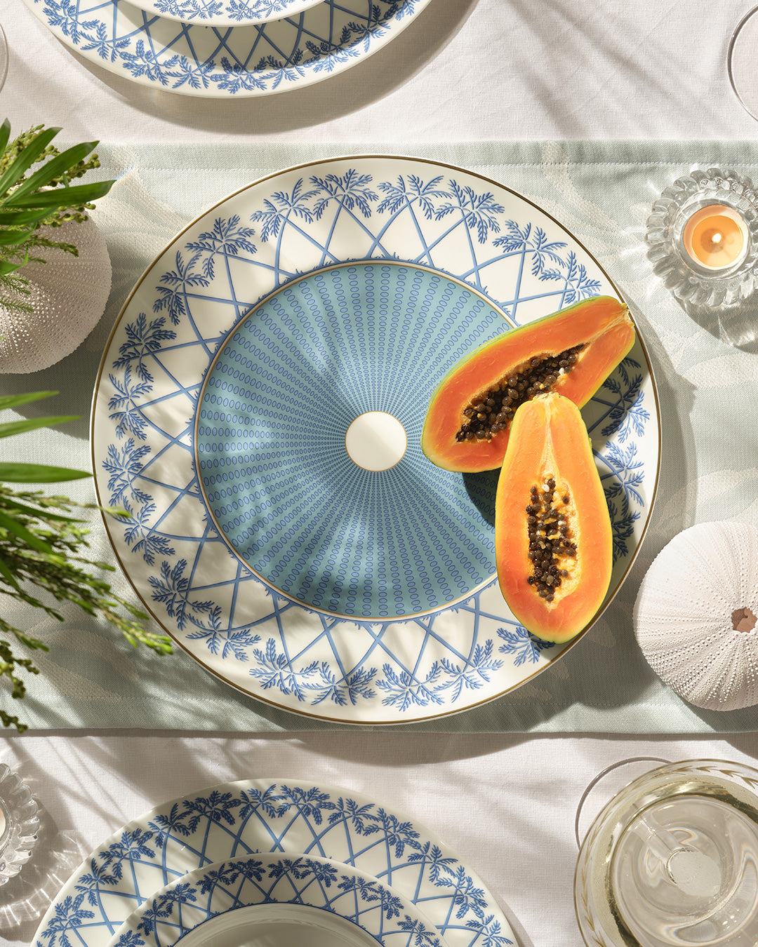 Tropical fine bone china charger plate with gold rim in Palms Azure blue, styled with fresh papaya for a Caribbean dining setting by Pink House Mustique