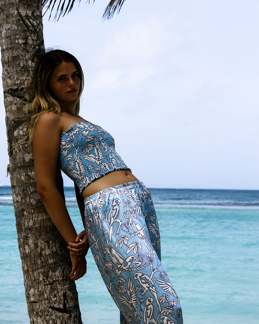 Silk bandeau and parrot blue pajama bottoms styled against palm tree at Lagoon Bay, Mustique