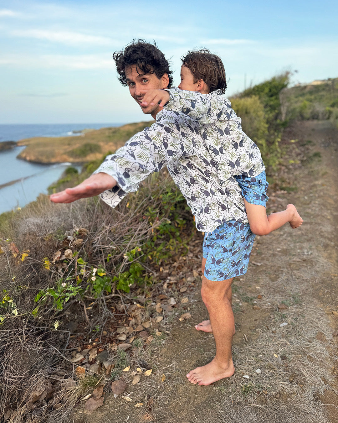 Playful father and child in coordinating Monkey & Palms linen shirts, family holiday mini-me style on the coast