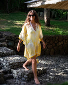 Woman wearing a yellow and white silk kaftan cover-up against a tropical background