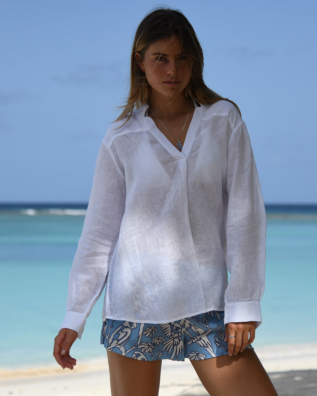 Model wearing silk Parrot print shorts in blue with white linen shirt, walking by the beach in Mustique