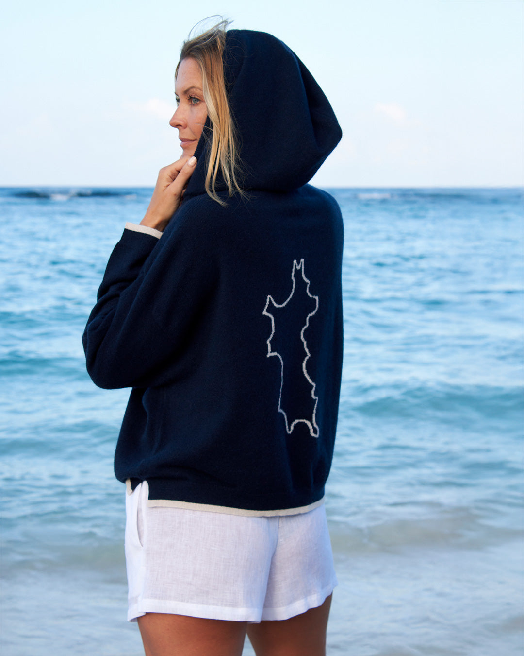 Malin modeling luxury cashmere navy blue hoodie with Mustique Island motif by Pink House x Darlin London, beachwear style on Mustique Island