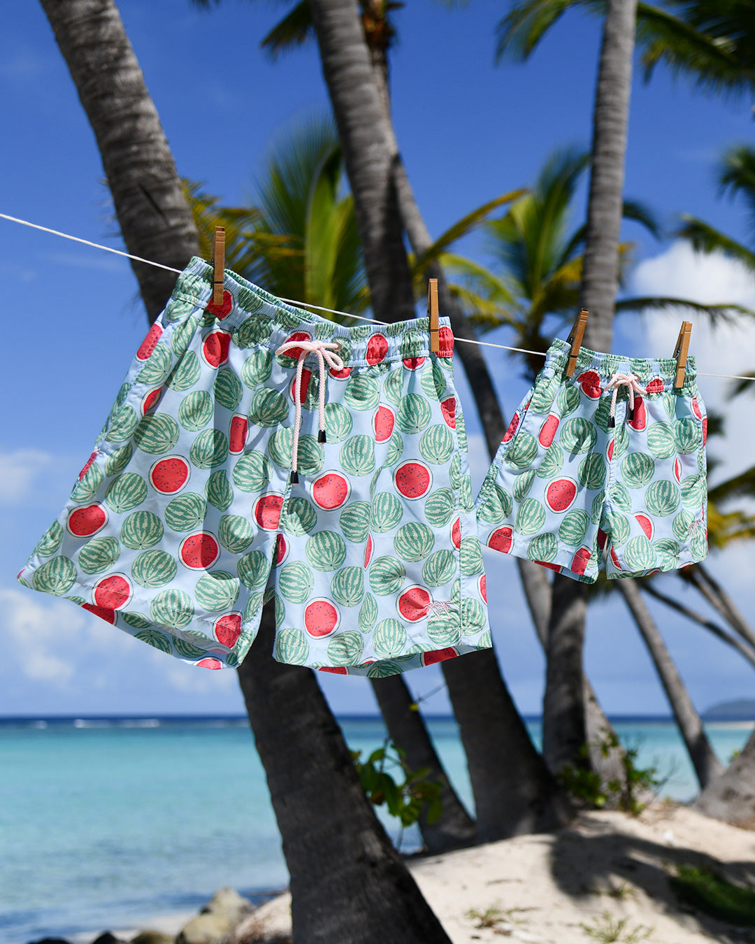 Men's and boys' Watermelon print swim shorts hanging beneath palm trees by the Caribbean sea