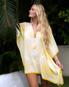 Woman wearing a yellow and white silk kaftan cover-up against a tropical background