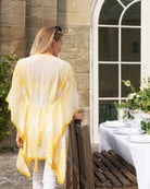 Woman in a yellow and white patterned cover-up standing near a table set outdoors.