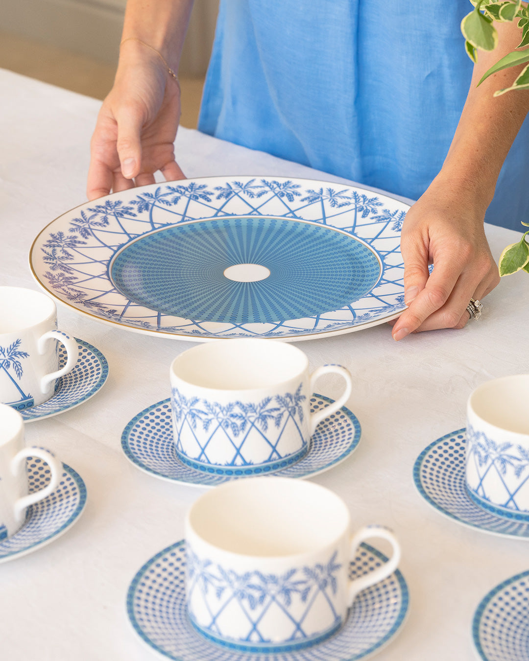 Luxury fine bone china charger plate with gold rim in Palms Azure blue, styled with matching teacups and saucers by Pink House Mustique