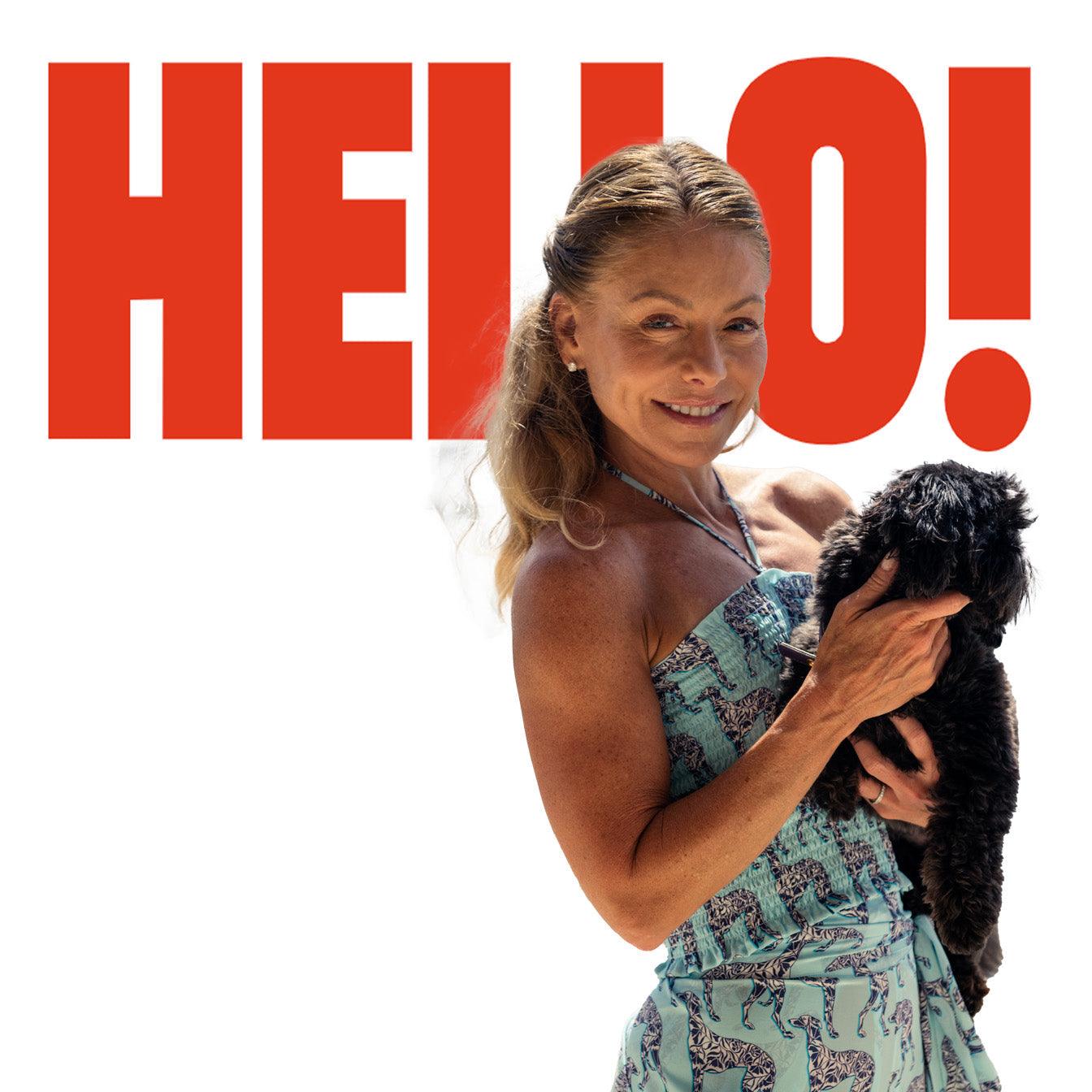 Smiling woman in patterned dress holding black dog, large HELLO! text in background.