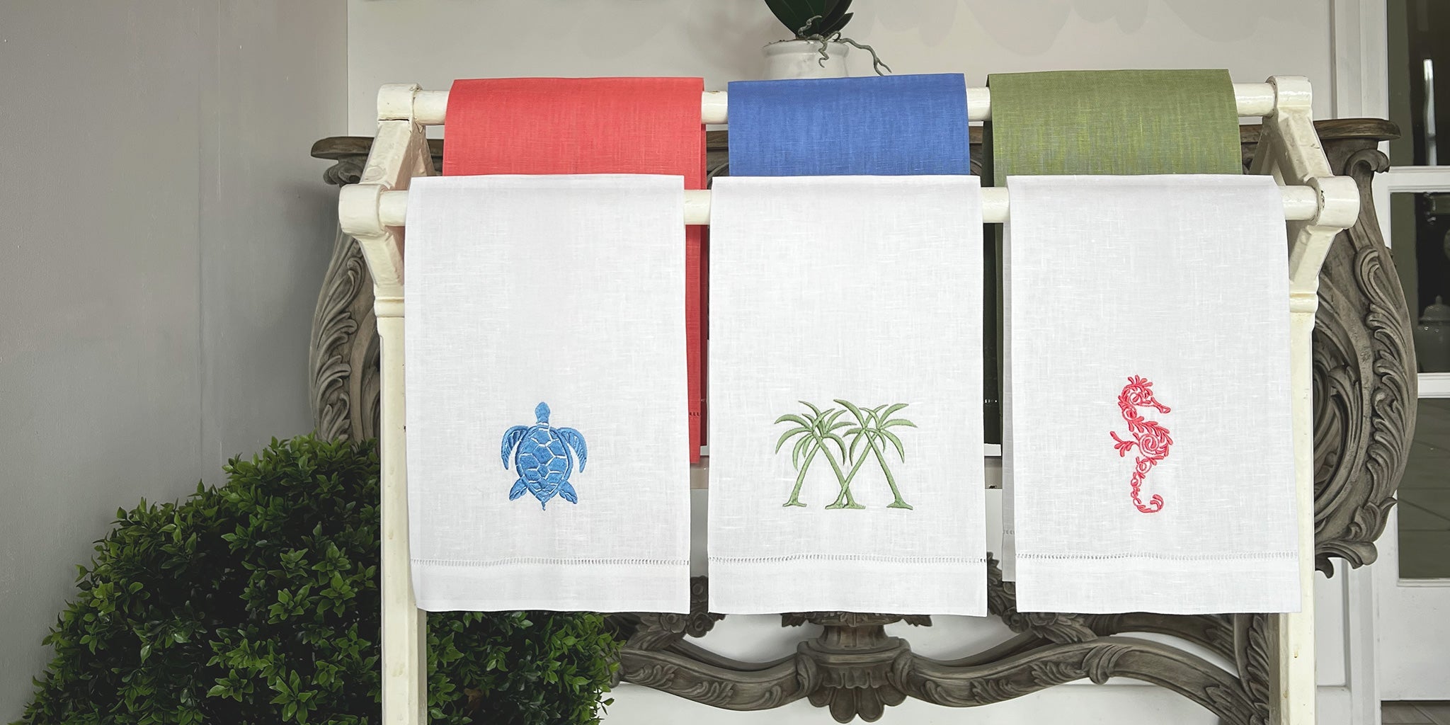 New in - Coloured linen hand towels with embroidered seahorse, palm, and turtle motifs displayed in Pink House Mustique showroom.