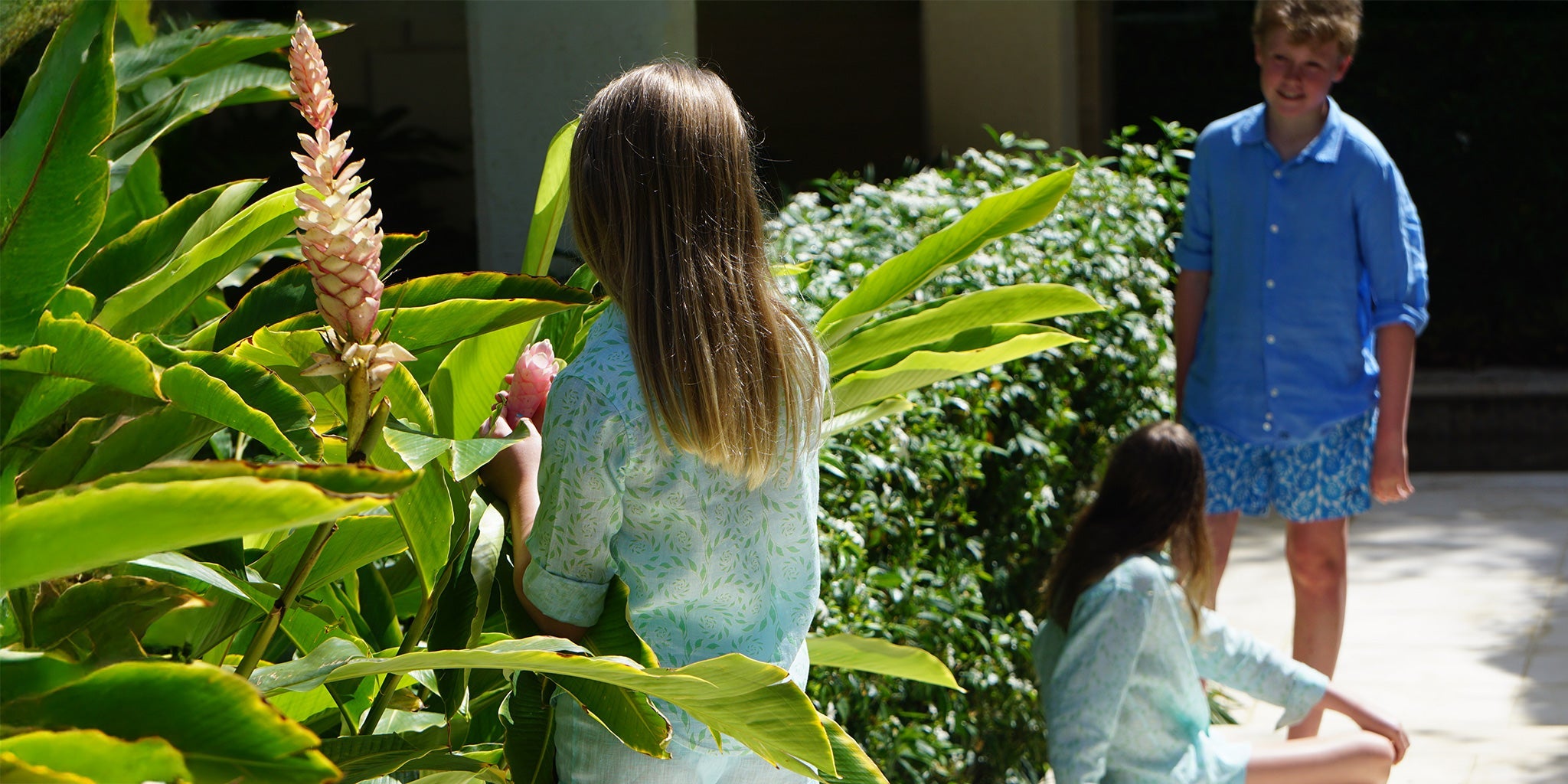 Children wearing Pink House kids linen shirts and swim shorts in a tropical garden, now on sale in the outlet