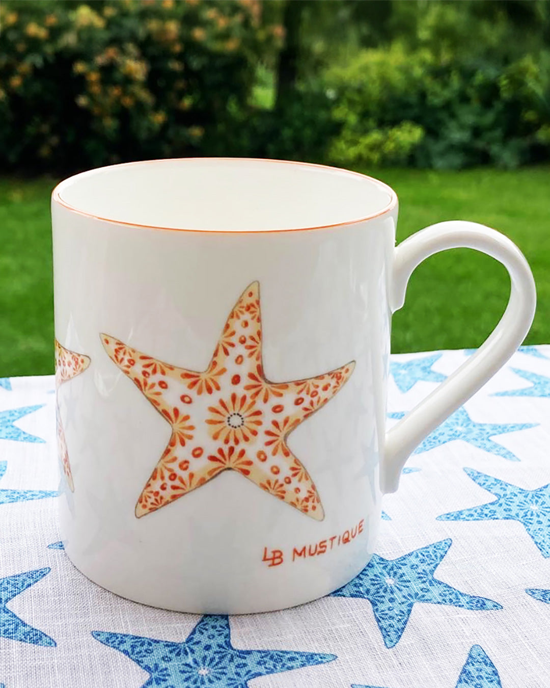 Lotty B orange Seastar fine bone china mug styled on matching starfish tablecloth in an English country garden.