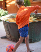 Back view of Frigate Bird Blue boys swim shorts worn with orange linen shirt