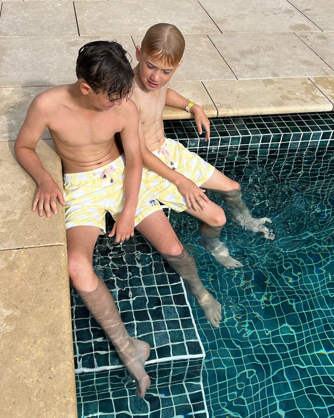 Boys wearing yellow Fan Palm swim shorts sitting at the edge of a swimming pool