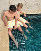 Boys wearing yellow Fan Palm swim shorts sitting at the edge of a swimming pool
