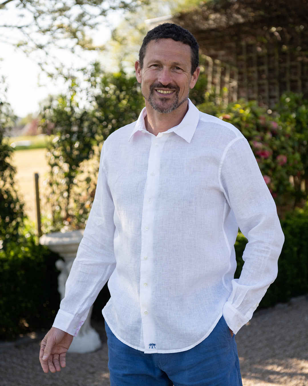 Man wearing Pink House Mustique Classic White Linen Shirt – long sleeve button-up shirt in breathable OEKO-TEX certified linen, styled with blue shorts for timeless summer resortwear.