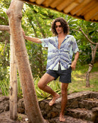 Jules wears silk Banana Tree Blue festival shirt with navy swim shorts – relaxed summer style by Pink House Mustique.