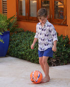 Kids unisex linen shirt in monkey and palms print, plum navy and green, styled with shorts at a luxury island villa