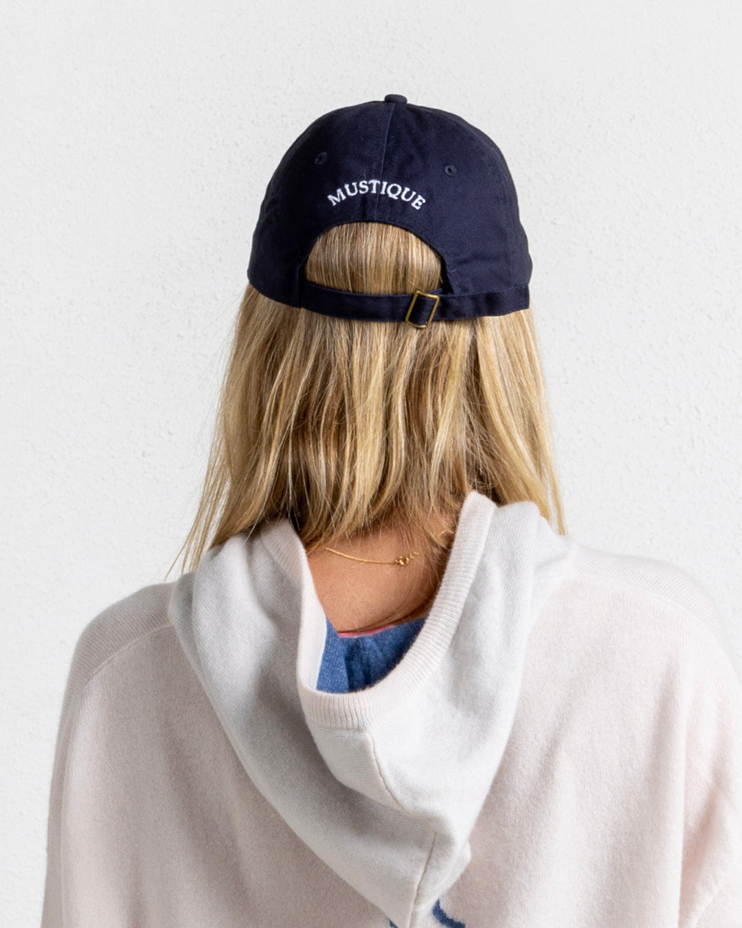 Navy baseball cap with white Mustique embroidery, adjustable strap, styled with cashmere hoodie for luxury island look.