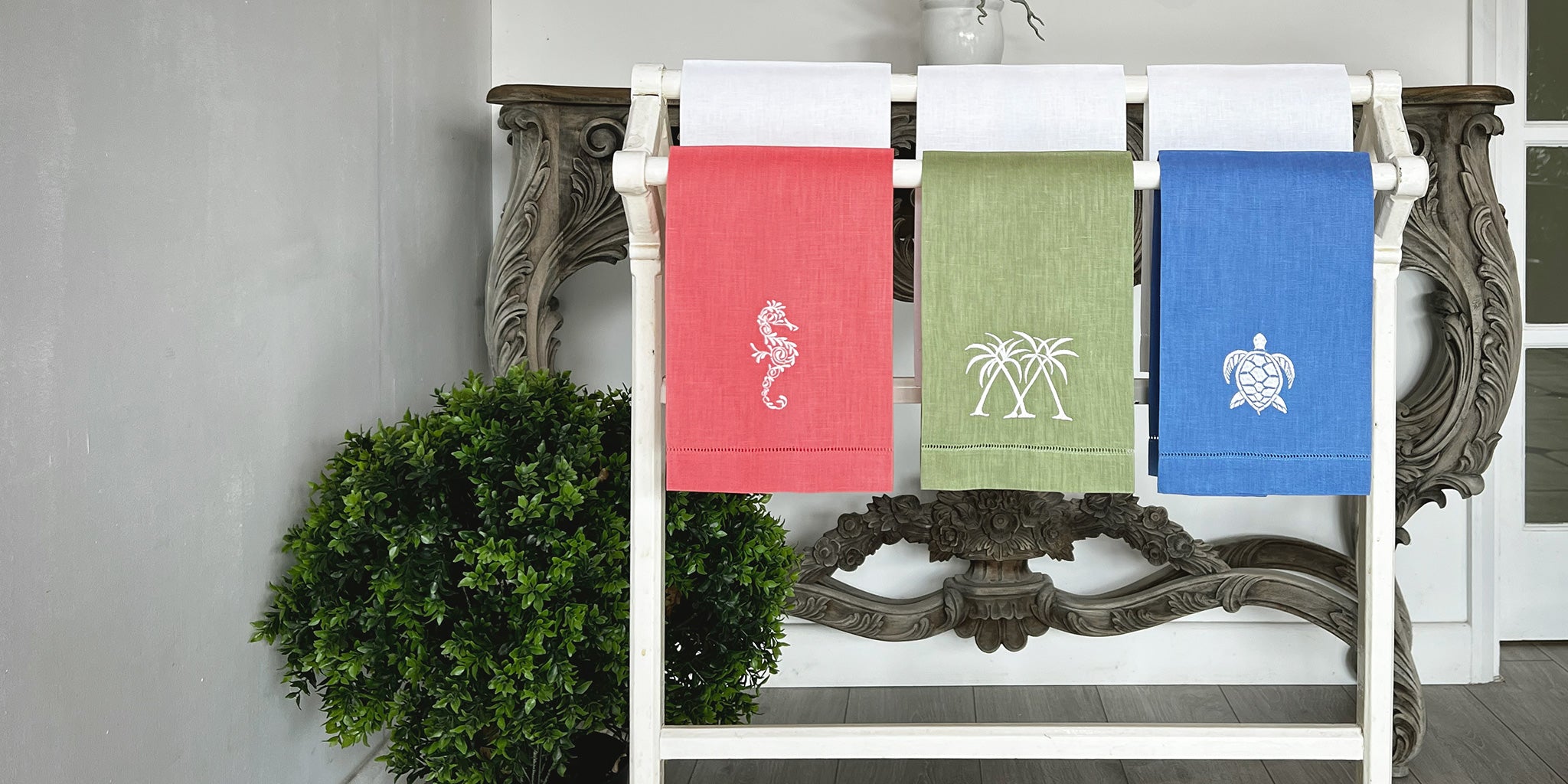Coloured linen hand towels with embroidered seahorse, palm, and turtle motifs displayed in Pink House Mustique showroom.