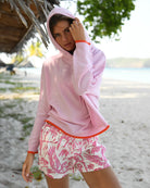 Lottie modelling Darlin London x Pink House Mustique cashmere hoodie in Mustique Island pink with orange trim on Lagoon Beach