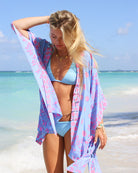 Milla wearing Lotty B Jade Poncho in Lime Tree Blue and Pink over a turquoise bikini – luxurious silk resortwear with tropical lime print, perfect for beach vacations and summer styling.